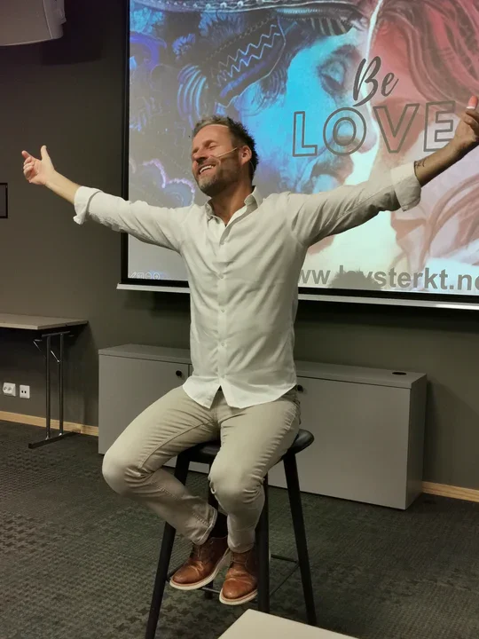 Kevin Frøystad med åpne armer på scenen foran en Lev Sterkt-skjerm